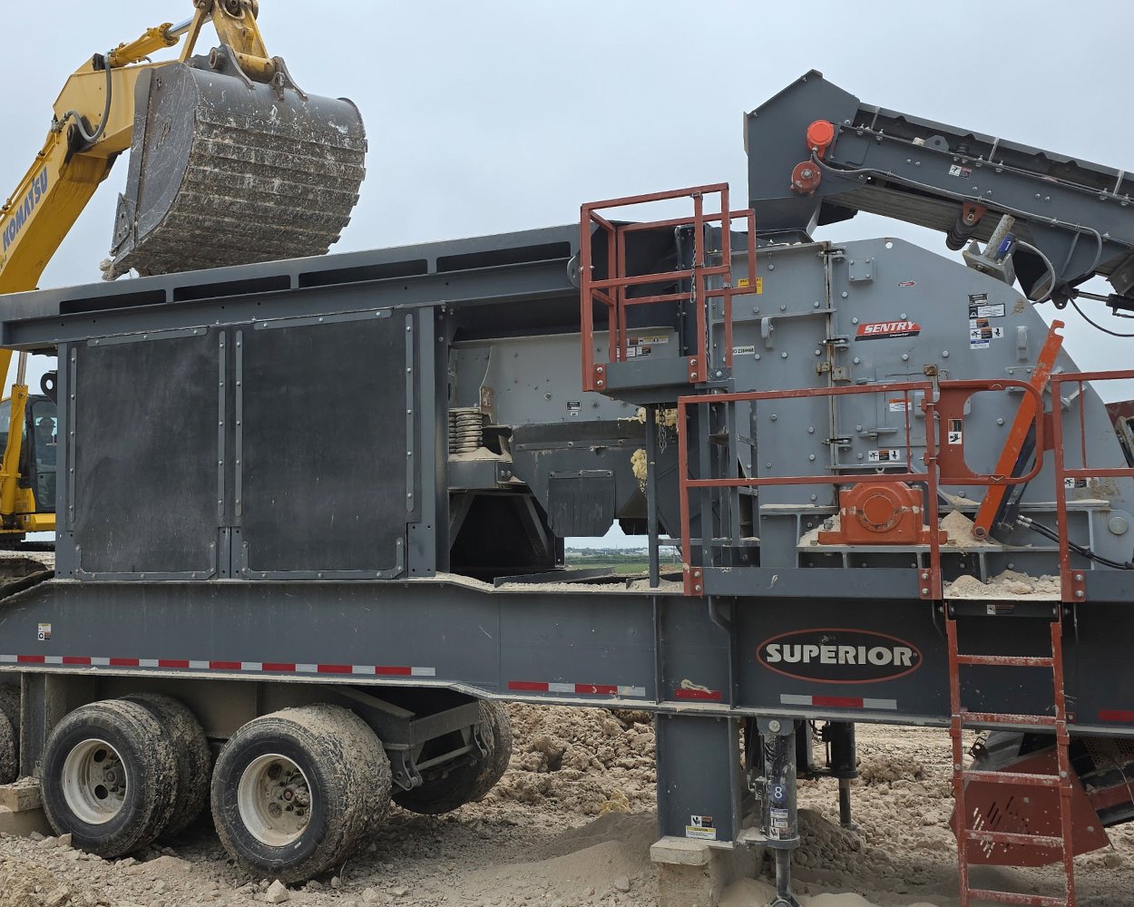 Portable Superior HSI crushing plant at a jobsite with an excavator loading material into the feed hopper.