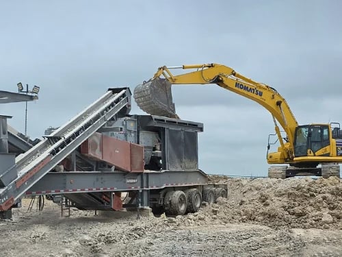 Excavator loading rock into a Superior Sentry® HSI portable crushing plant at an aggregate processing site.