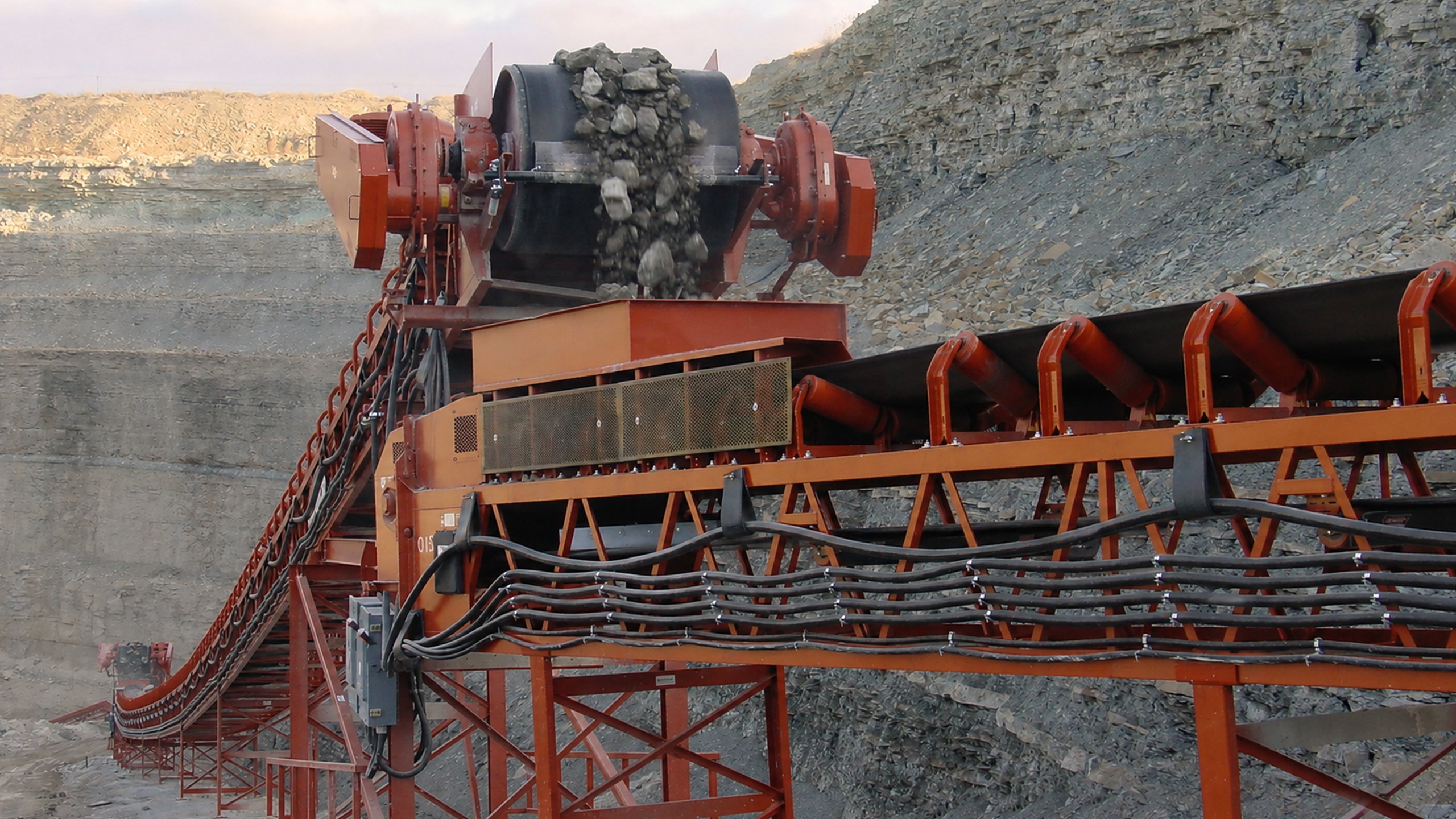Crushed stone discharging from a transfer chute onto a belt conveyor at an aggregate processing plant.