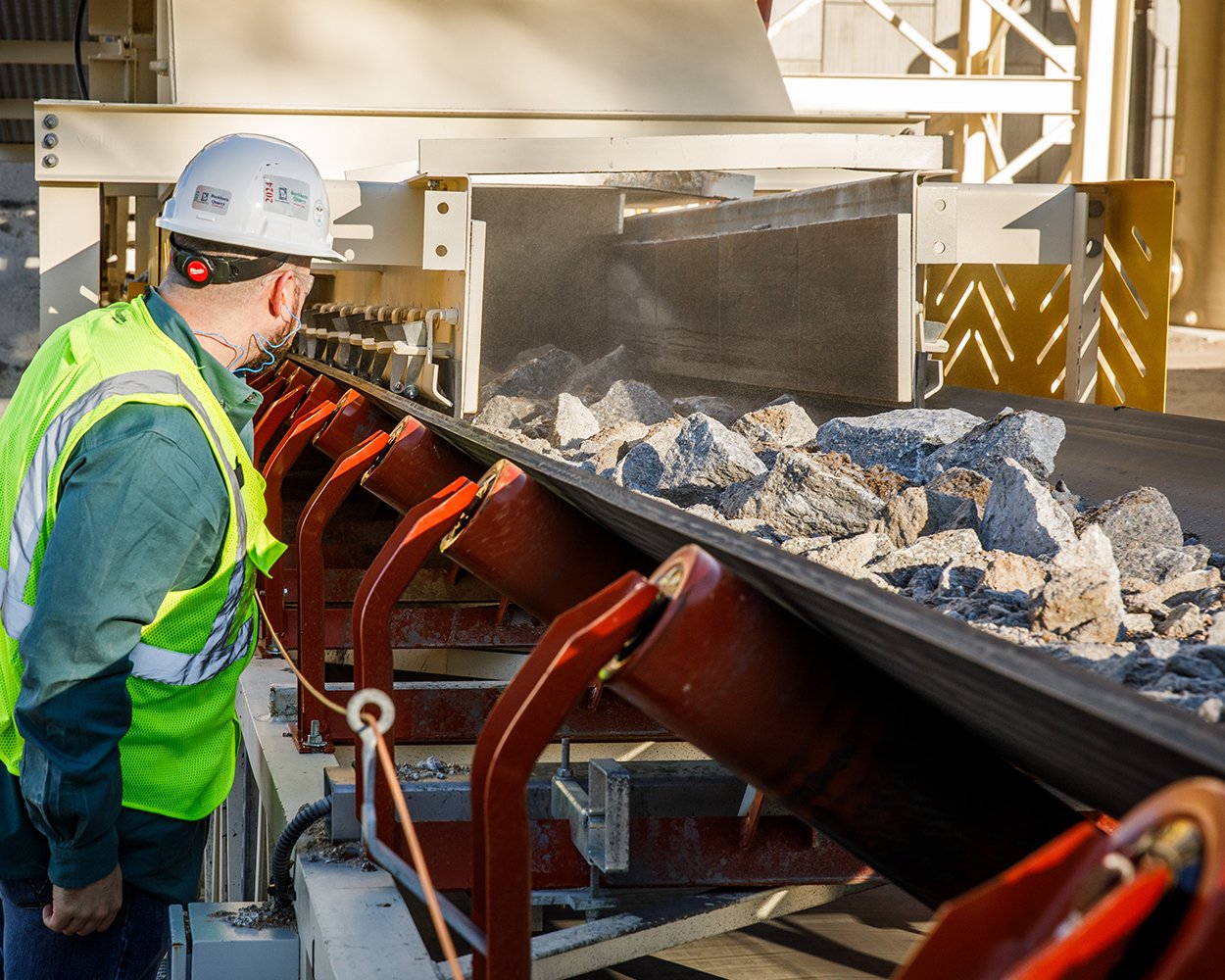 Worker inspecting conveyor idlers at a rock transfer point