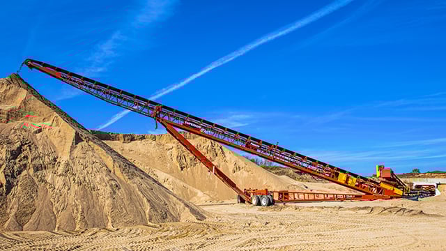 Superior® Radial Stacking Conveyor creating a large sand stockpile at a quarry site, featuring mobile radial movement for high-volume material handling.