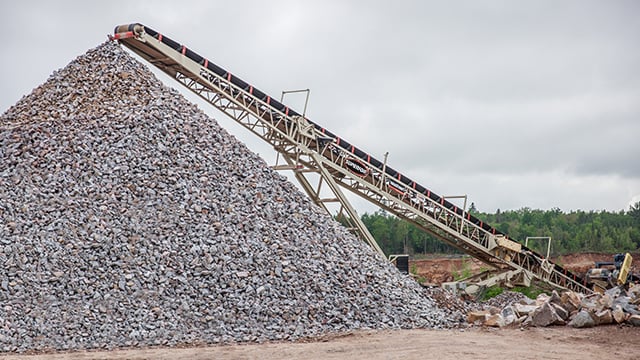 Superior® Radial Stacking Conveyor depositing sand into stockpiles at a quarry site surrounded by rock walls and trees.