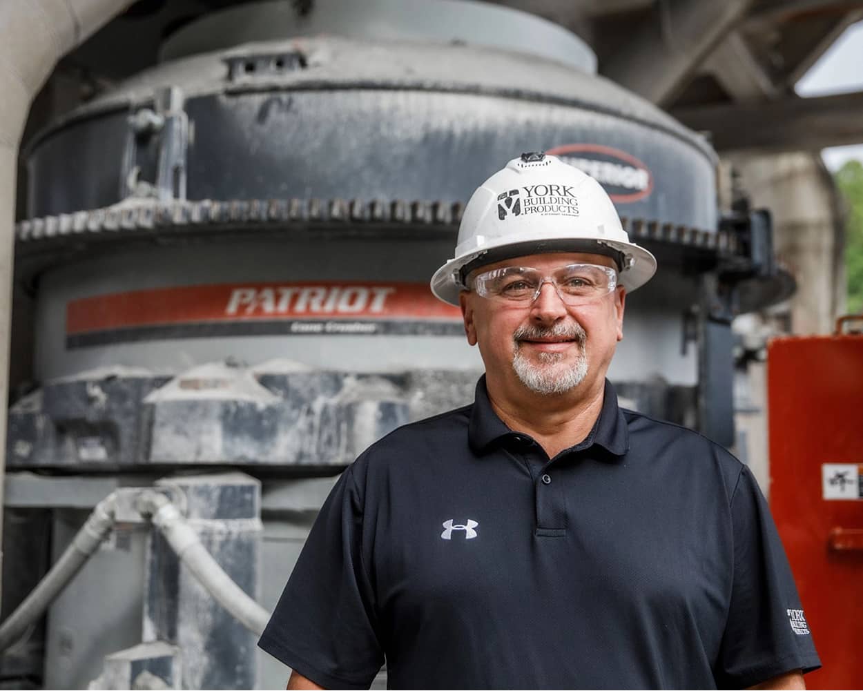 Man wearing a hard hat stands in front of a Patriot Cone Crusher at York Building Products in Thomasville, Pennsylvania.