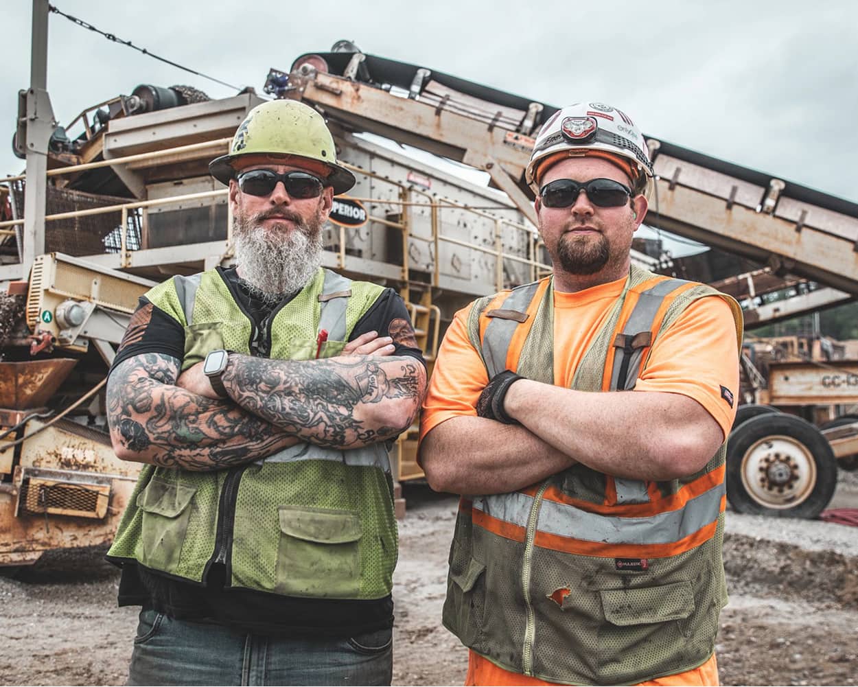Two workers in safety gear stand confidently in front of a portable horizontal screen at a quarry site in Iron Mountain, Michigan