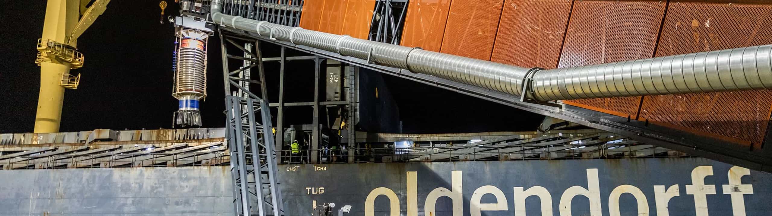 TeleStacker® Conveyor loading a ship with wood pellets at night.