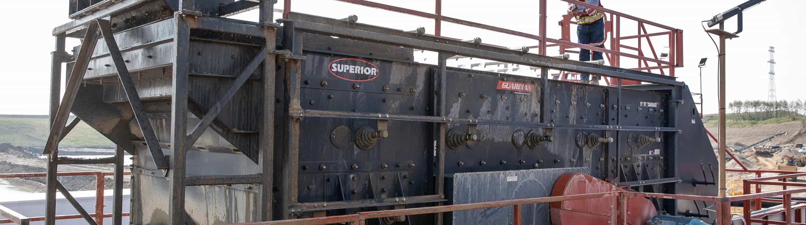 Triple shaft horizonal screen Guardian Screen in operation at Calgary wash plant, fed by conveyor, operator watching feed, hanging onto plaform