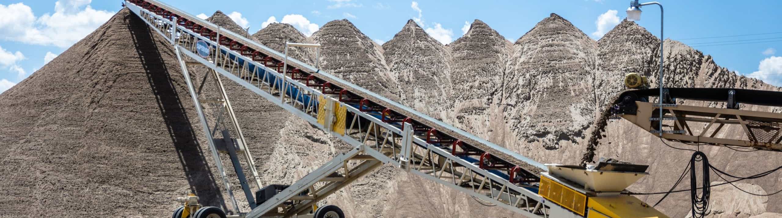 Superior® Portable Radial Stacker in operation stockpiling a serious pile of sand, fed by a second conveyor