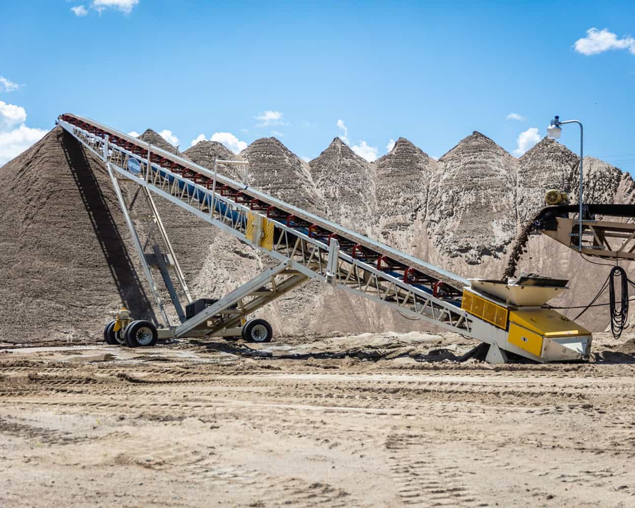 Portable Radial Stacker in operation stockpiling large sand pile fed by secondary conveyor