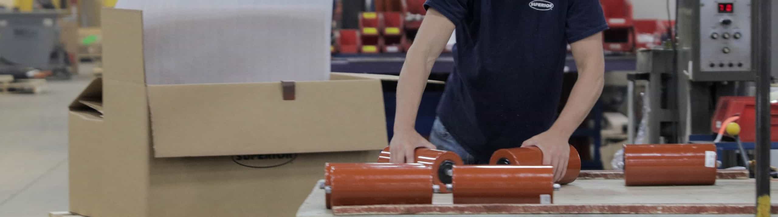 Employee at Superior manufacturing plant preparing replacement steel idler rolls for shipment