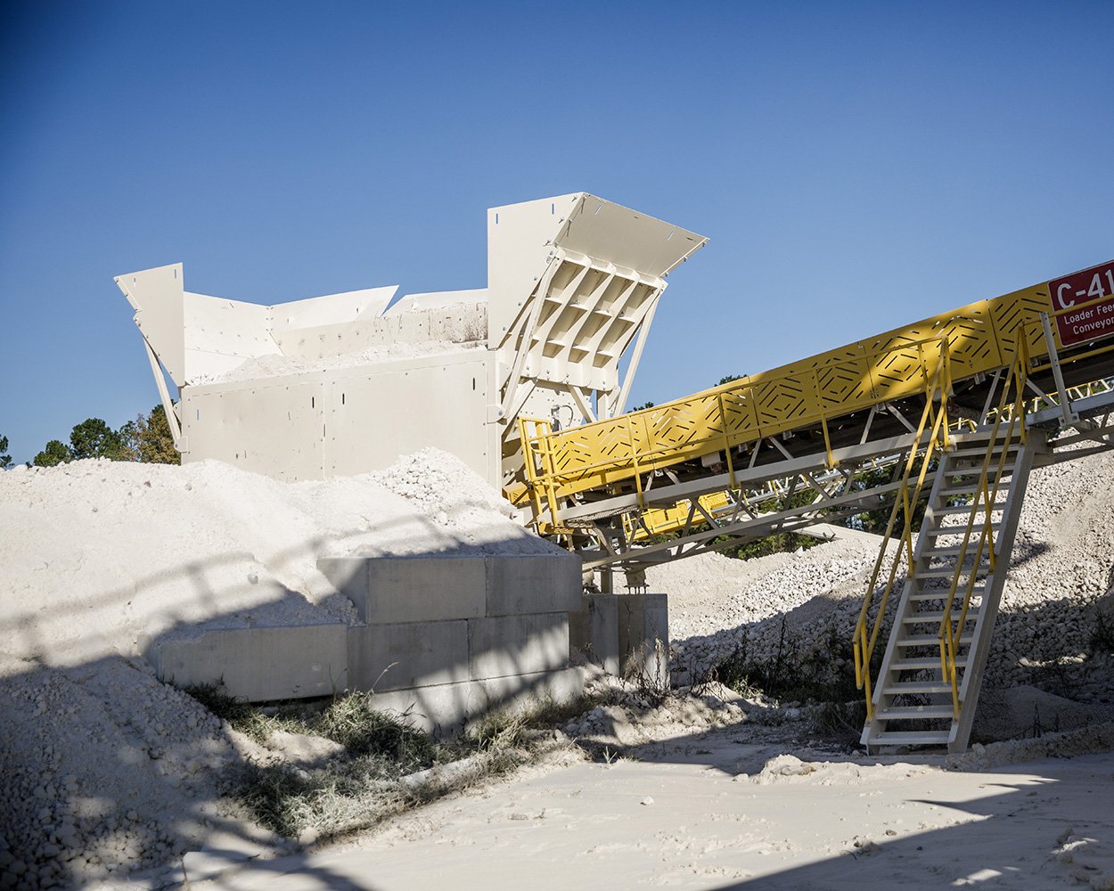 Payloader feeding aggregate into conveyor through stationary feed hopper