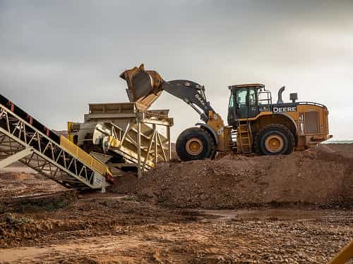 Payloader feeding aggregate into conveyor via stationary feed hopper