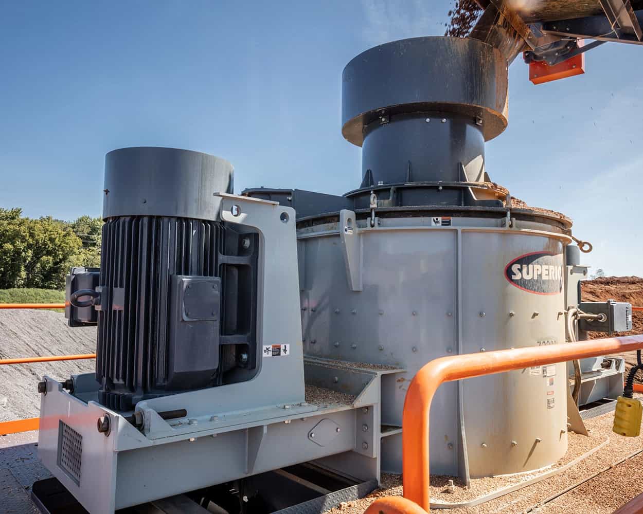 Material feeding into Superior® Cemco® VSI Crusher under clear blue sky producing spec material on-site