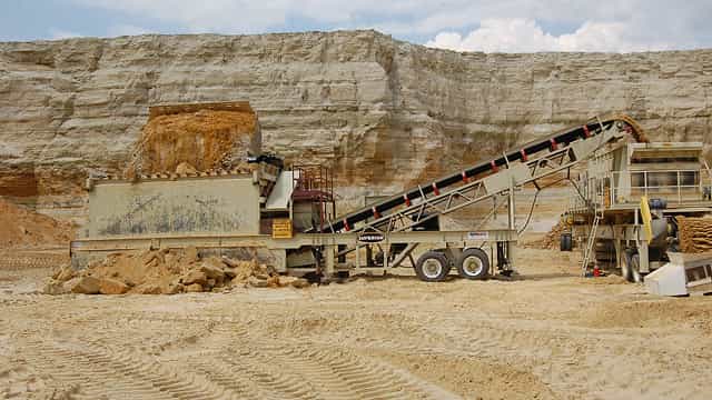 Superior® portable feed hopper and conveyor system operating at a sand quarry, controlling material flow from stockpile to processing equipment.