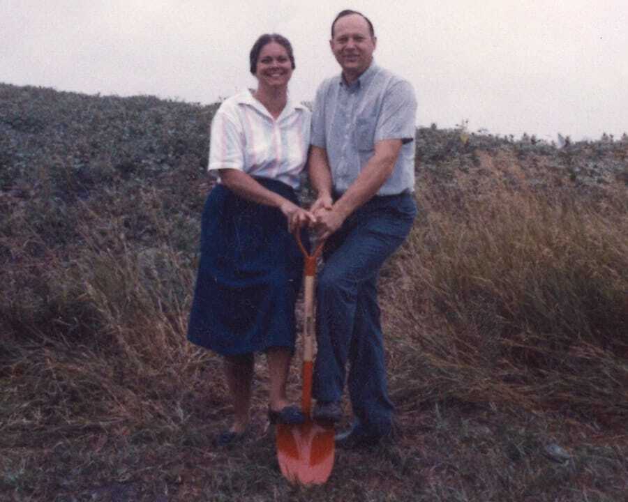 Neil and Linda Schmidgall stand together on grassy ground holding a shovel.