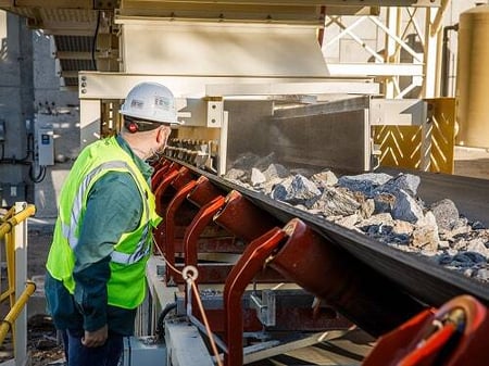 An engineer wearing a hard hat and safety vest inspects a conveyor system carrying crushed rock, illustrating Superior’s hands-on approach to engineering and design