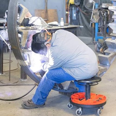 A welder in protective gear works on a large steel crusher component inside Superior’s Belen, New Mexico facility