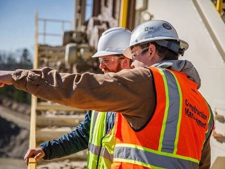 Two field technicians wearing safety vests and hard hats discuss maintenance plans beside operating equipment, representing Superior’s ongoing lifetime support for plant owners