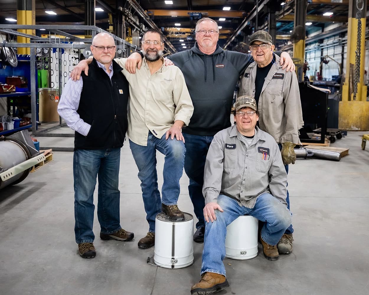 Five longtime Superior Industries employees stand together inside a manufacturing facility, celebrating more than 35 years of service with the company.