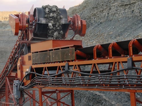 Crushed stone discharging from a transfer chute onto a belt conveyor at an aggregate processing plant.