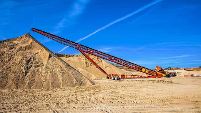 Superior® Radial Stacking Conveyor creating a large sand stockpile at a quarry site, featuring mobile radial movement for high-volume material handling.