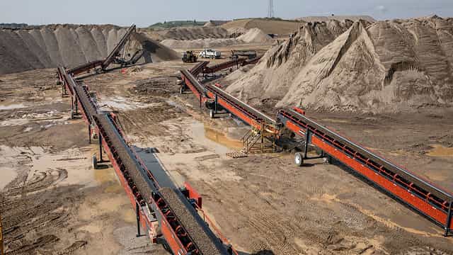Multiple Superior® Portable Transfer Conveyors moving sand and gravel between stockpiles at a large open quarry site.