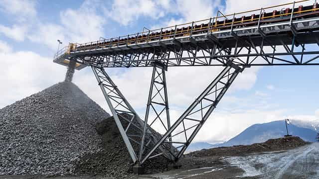 Superior® Stationary Stacker conveyor depositing crushed rock into a large stockpile at a quarry with mountains in the background.