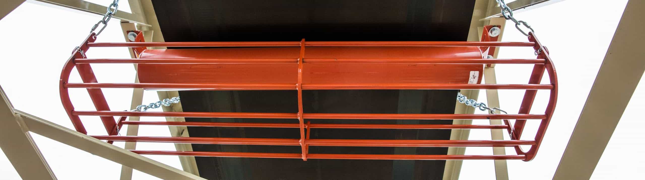 Return idler basket guarding steel return roll on aggregate conveyor, positioned beneath the belt