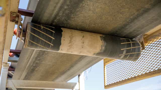 Close-up view of a Superior® Training Idler guiding a conveyor belt for precise alignment and tracking during aggregate material transport.