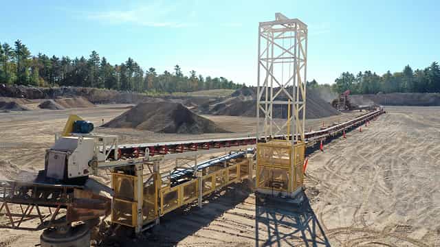Superior® Stationary Transfer Conveyor system moving aggregate material across a large quarry site with multiple stockpiles in the background.