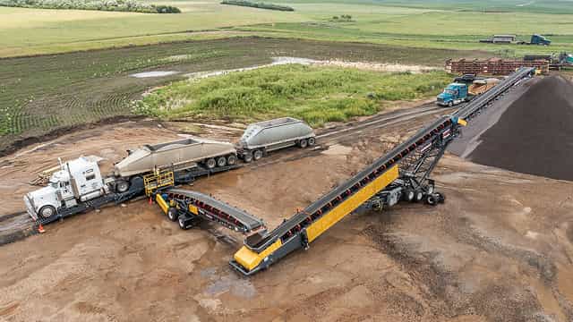 Superior® RazerTail® Truck Unloader transferring material from haul trucks to a radial stacking conveyor at an open-site aggregate operation.